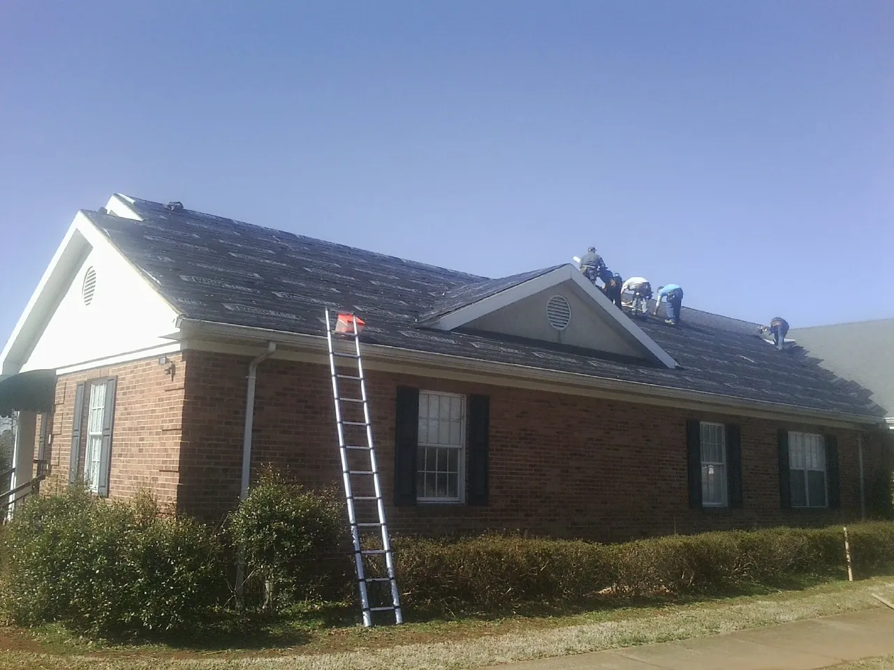 Crew tearing shingles off a brick ranch roof with a ladder set — Emergency Roof Repair work by our crew in Saint Michaels