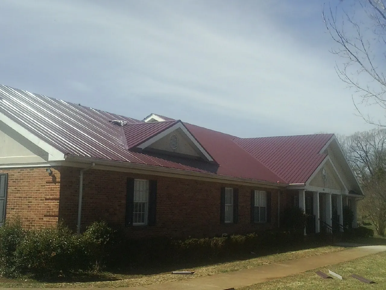 Red metal roof with gabled entries on a long brick building, from a Hail Damage Roof Repair job in Saint Michaels