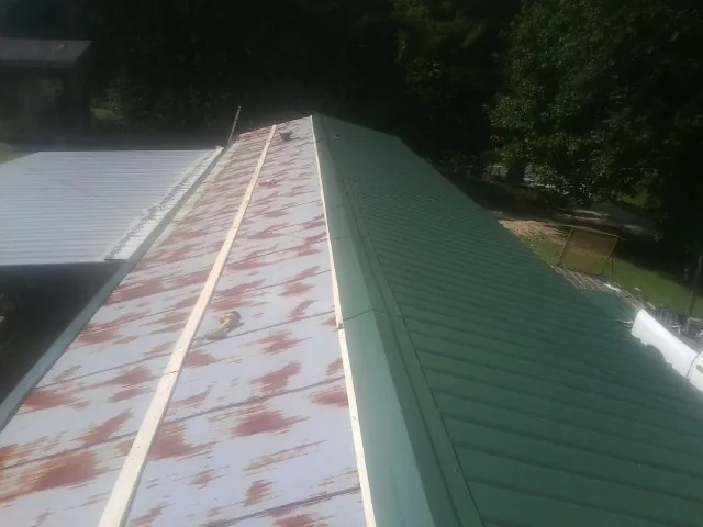 Old rusted panels beside newly installed green metal roofing — Wind Damage Roof Repair by Roofing Brothers in Saint Michaels