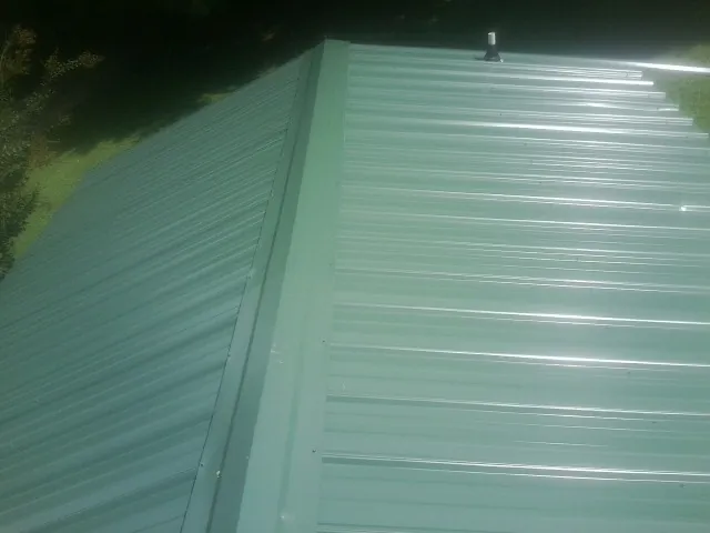 New green metal panels meeting at the ridge of a roof — Flat Roof Repair work by our crew in Saint Michaels