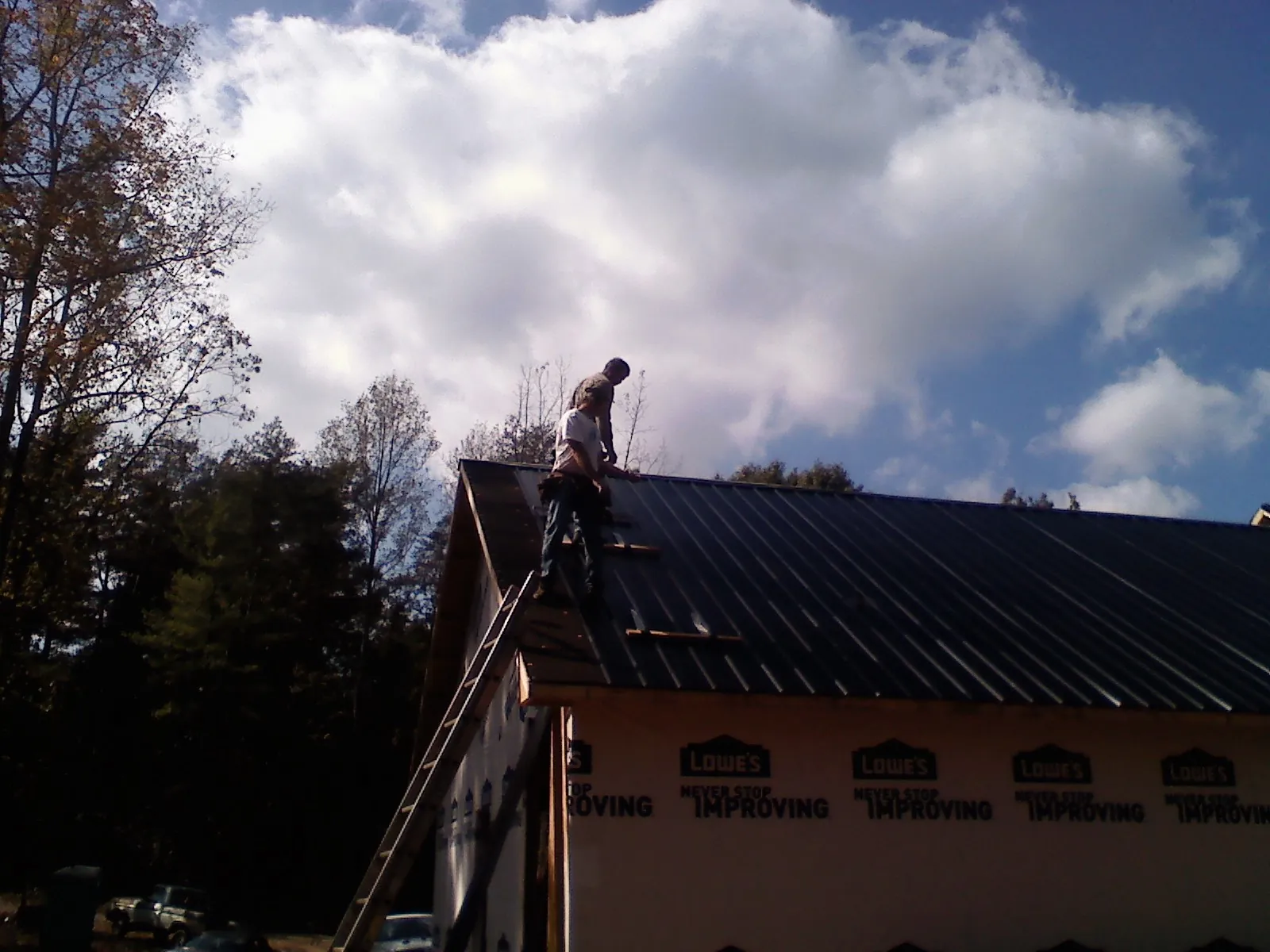 Roofer fastening dark metal panels high against a cloudy sky, from a Roof Inspection job in Saint Michaels