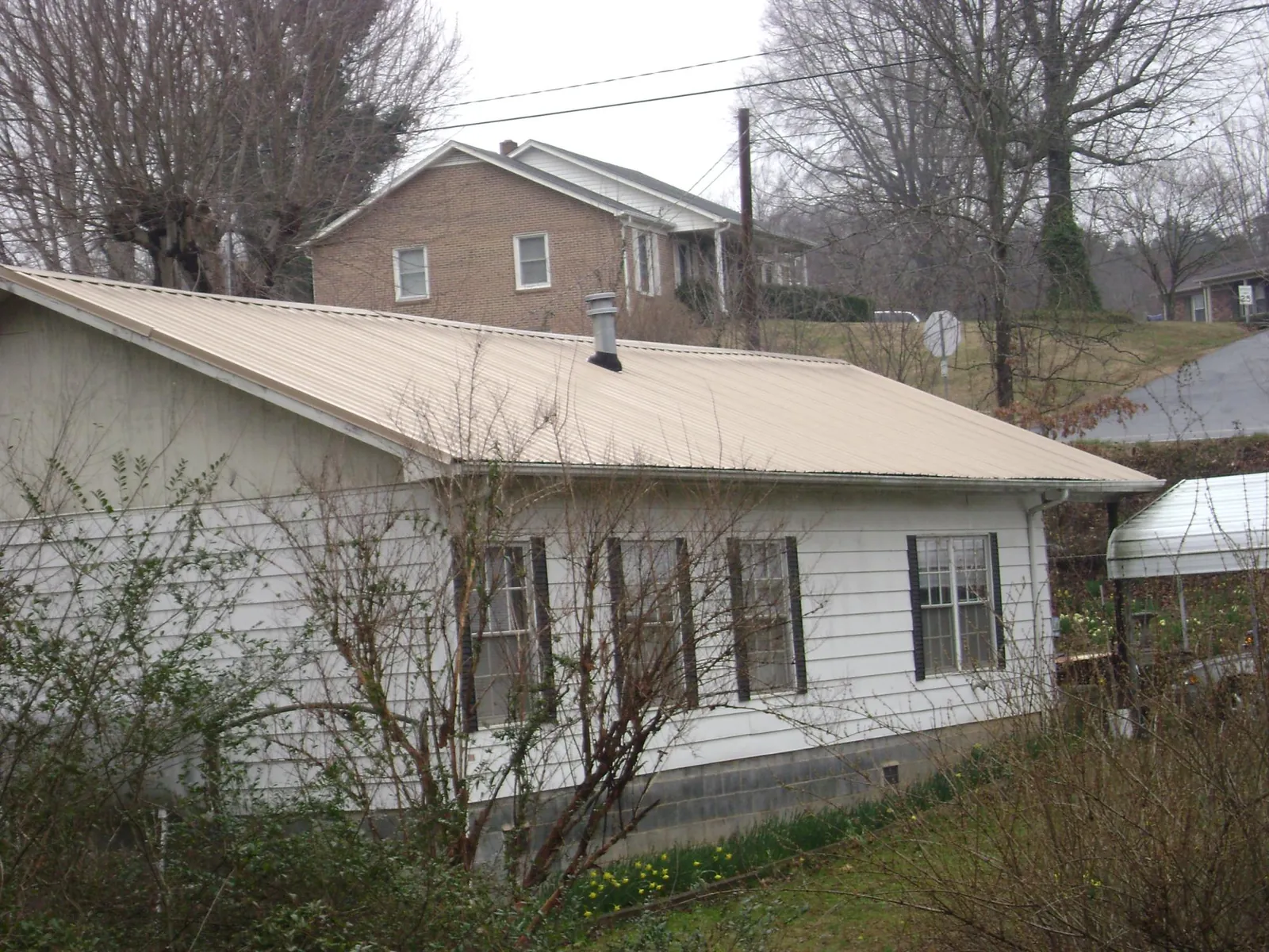 Tan metal roof on a white sided house set into a hillside — Commercial Roofing by Roofing Brothers in Saint Michaels